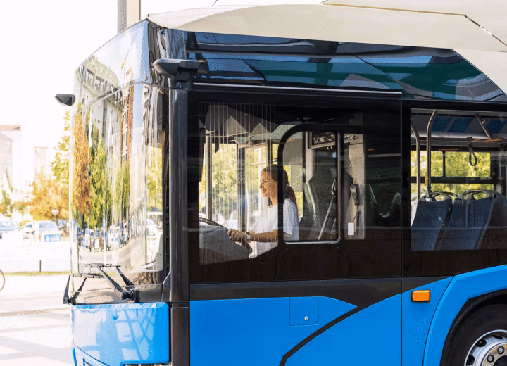 Motorista ao volante de ônibus urbano azul parado em rua arborizada, vista lateral da cabine