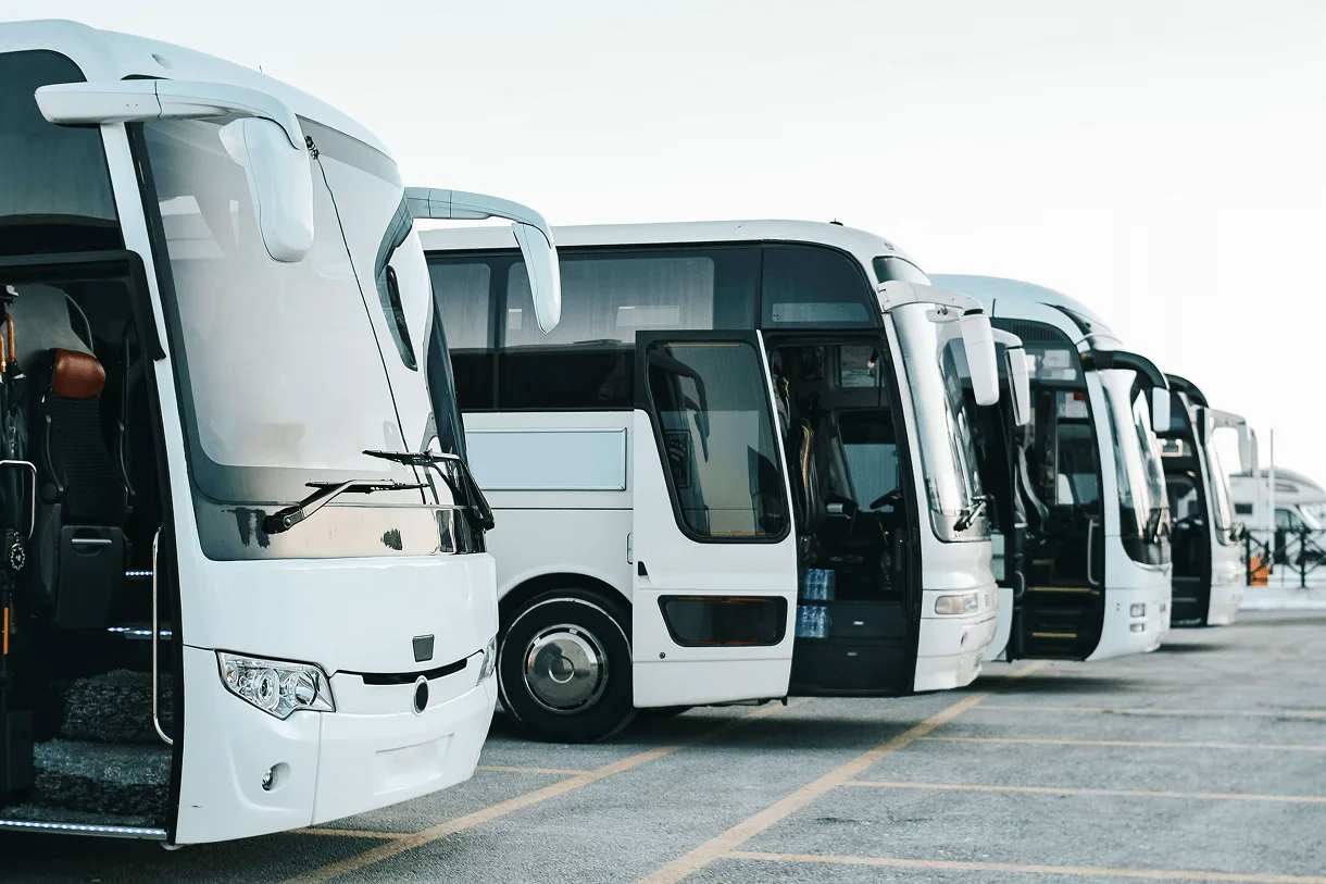 Fileira de ônibus rodoviários brancos estacionados lado a lado em pátio, com portas dianteiras abertas