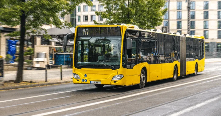 Ônibus urbano articulado amarelo com o letreiro 147 trafegando por avenida entre prédios