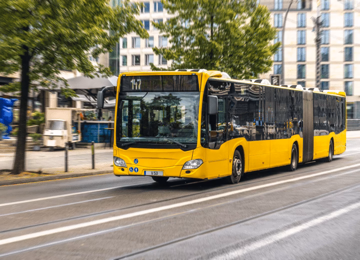 Ônibus urbano articulado amarelo com o letreiro 147 trafegando por avenida entre prédios
