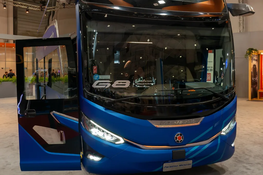 Frente de um ônibus de dois andares Marcopolo Paradiso G8 azul, com o emblema G8 no para-brisa e a porta aberta, em exposição na feira Busworld Europe 2023