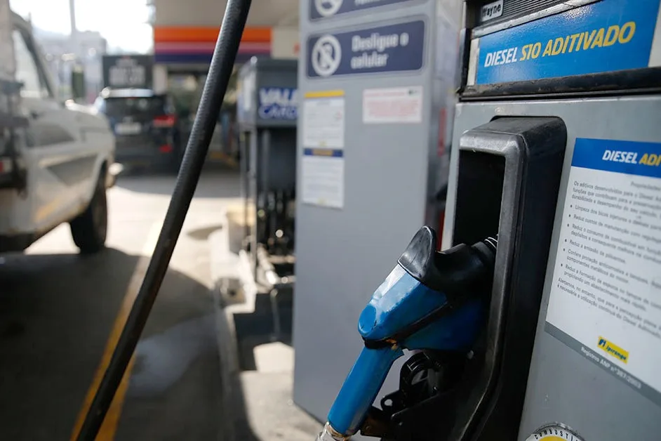 Bico de abastecimento azul em bomba de diesel S10 aditivado em um posto, com uma caminhonete ao fundo