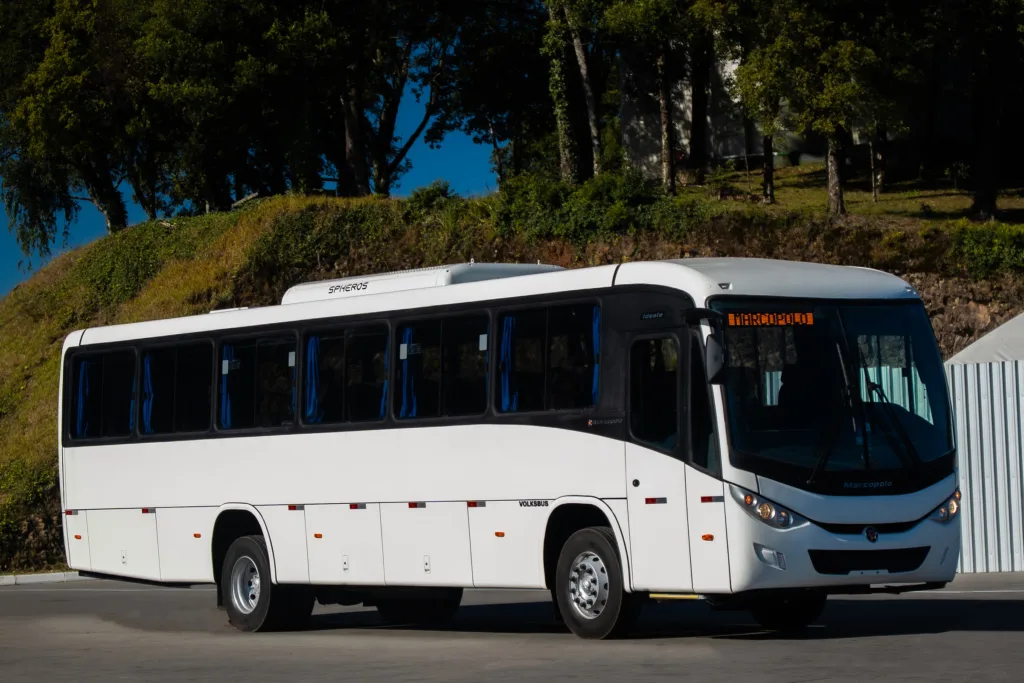 Ônibus Marcopolo Ideale branco sobre chassi Volksbus, visto de frente em três quartos diante de uma encosta com árvores