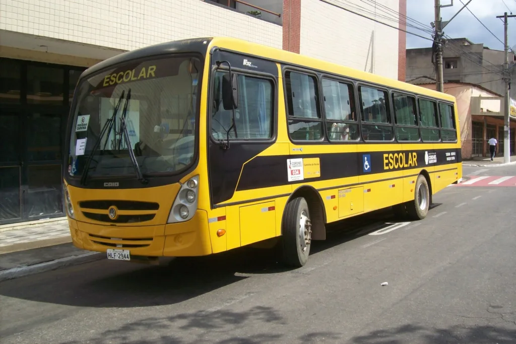 Ônibus escolar amarelo com faixa preta e o dístico ESCOLAR, parado numa rua de Coronel Fabriciano (MG)